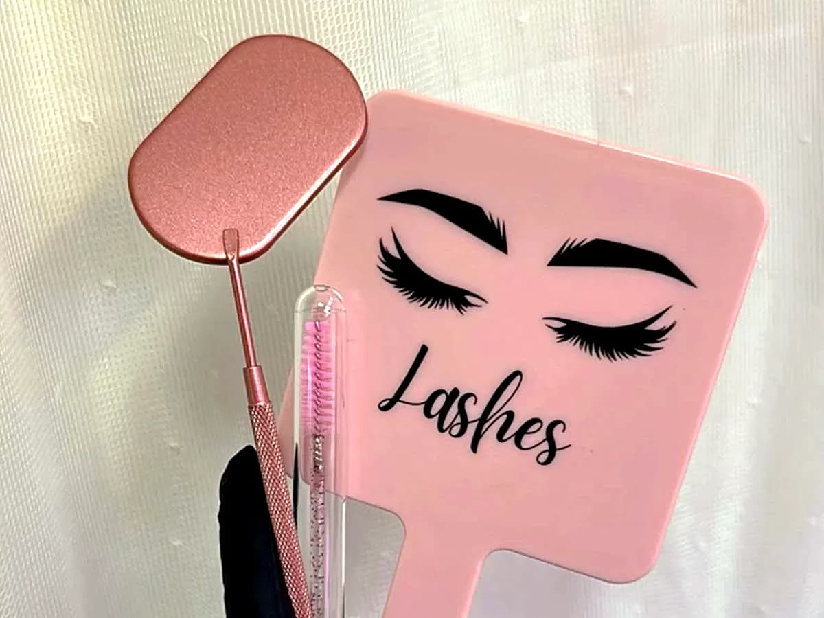 Pink lash mirror, lash brush and rose-gold lash tool held in a gloved hand