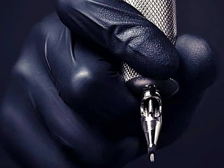 Gloved hand gripping a tattoo machine with the needle ready